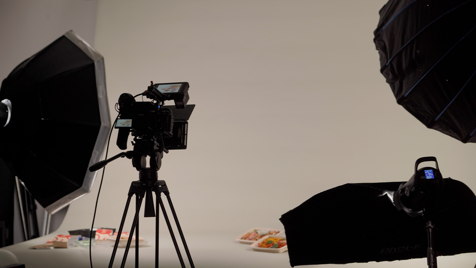 Video Agency: Image of studio setup, camera rig and lighting facing towards a beige backdrop with meal prep products on the backdrop.